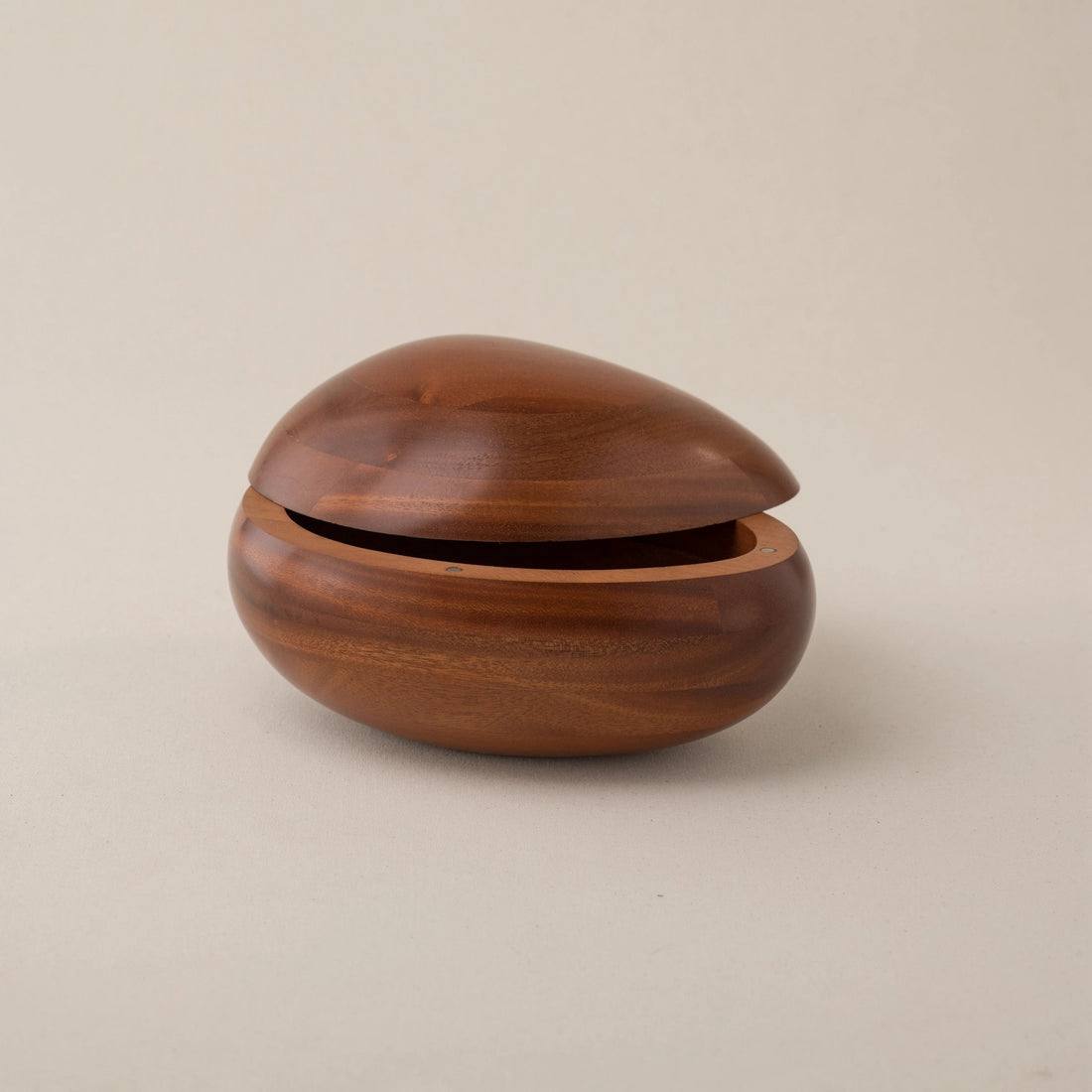 Urna de madera con forma de canto rodado, abierta, sobre un fondo neutro